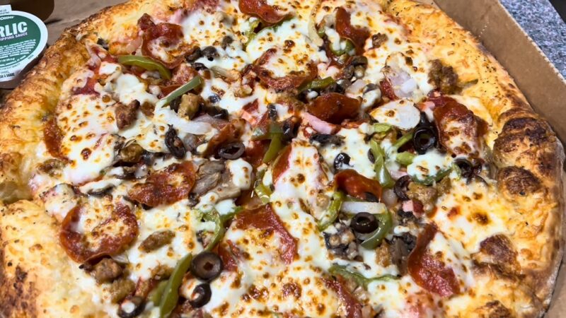 A loaded pizza with a variety of toppings, including pepperoni, onions, bell peppers, black olives, and sausage