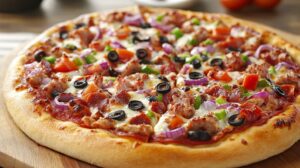 A freshly baked pizza topped with sausage, olives, red onions, green peppers, and melted cheese on a wooden board