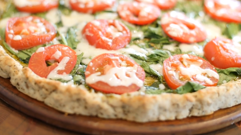 Freshly Baked Chicken Crust Pizza Topped with Spinach, Sliced Tomatoes, and Melted Cheese