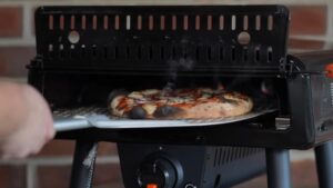 A Freshly Baked Pizza with Bubbling Cheese and Charred Crust Is Being Removed from A Blackstone Pizza Oven Using a Pizza Peel