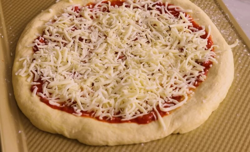 Preparing a classic cheese pizza, showcasing the even distribution of cheese over the sauce