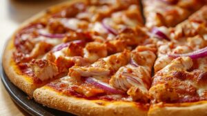 Close-up of a freshly baked barbecue chicken pizza with melted cheese, red onions, and a crispy crust on a black pan