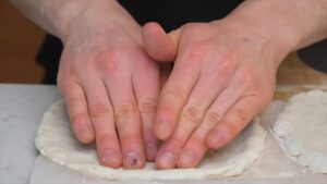 A Person Pressing and Shaping Gluten-Free Pizza Dough Into a Round Crust on Parchment Paper