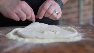 Hands Shaping and Stretching Pizza Dough on A Floured Wooden Surface