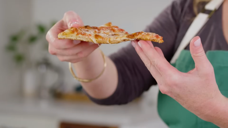 A Person Holding a Slice of Reheated Pizza with Melted Cheese