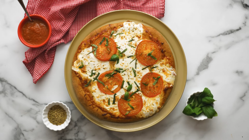 A Whole Wheat Crust Veggie Pizza Topped with Fresh Tomatoes, Basil, and Mozzarella Cheese, Served with Tomato Sauce and Oregano on The Side